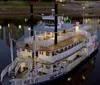 A traditional paddlewheel riverboat named Memphis Queen is navigating a river with a bridge and a pyramid-shaped structure in the background