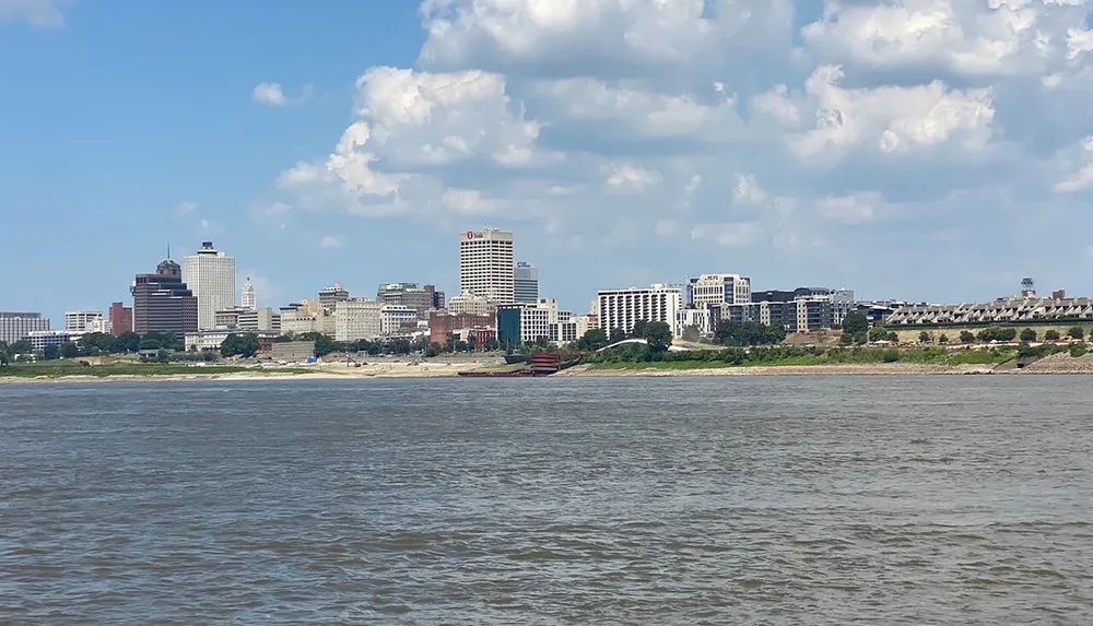 The image shows a scenic view of a city skyline as seen from across a river under a partly cloudy sky