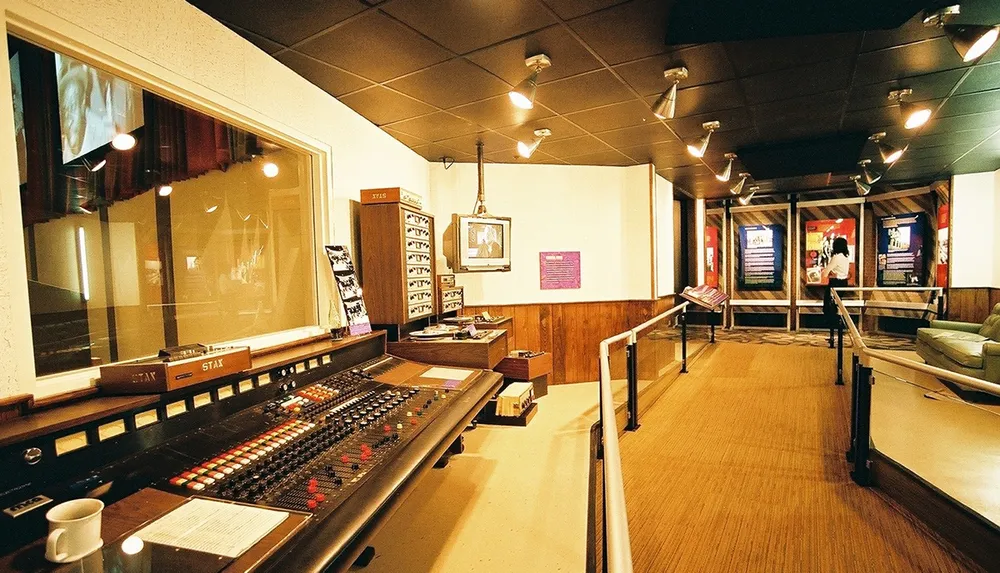 This image shows the interior of a vintage recording studio with a large sound mixing console in the foreground and what appears to be a framed picture and music memorabilia in the background