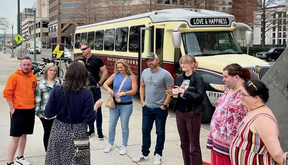 A group of people is standing in front of a tour bus labeled LOVE  HAPPINESS on a city street appearing to be either beginning or ending a tour
