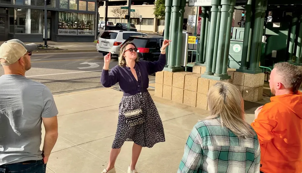 A person enthusiastically gestures during a conversation with three others on a sunny urban sidewalk