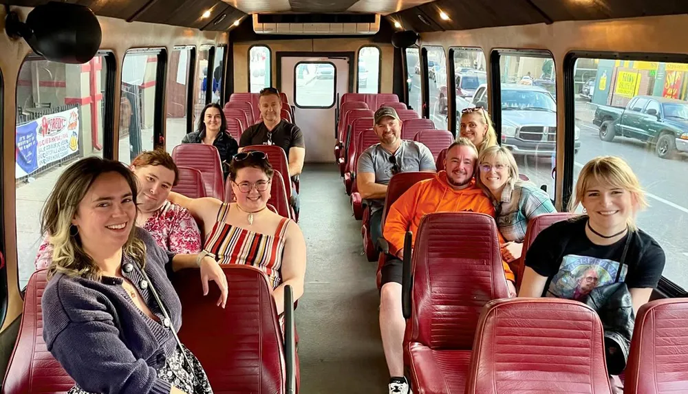 A group of smiling people is seated inside a spacious shuttle bus with red seats