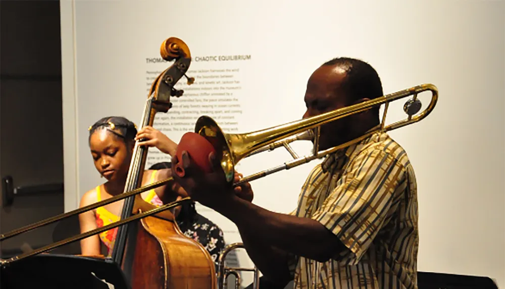 A man is playing a trombone while a woman plays a double bass in a music performance setting