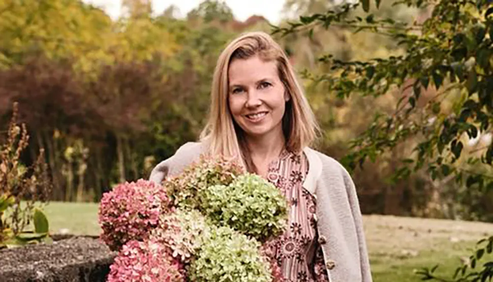 A woman smiles while holding a bouquet of hydrangeas in a garden setting