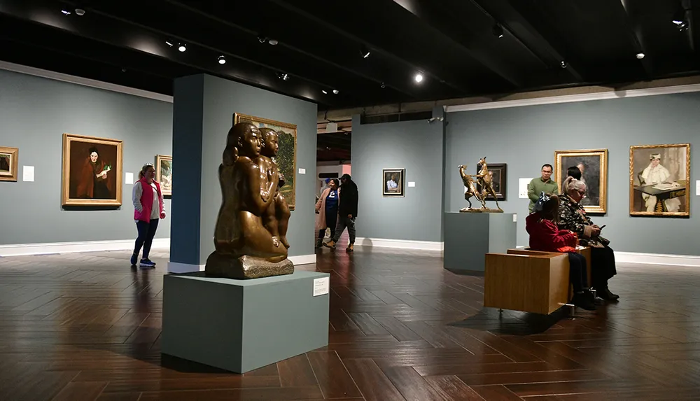 The image depicts visitors observing artwork and sculptures in an art gallery