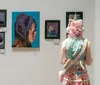 A person with pink hair and a whimsical outfit observes artwork displayed on a gallery wall