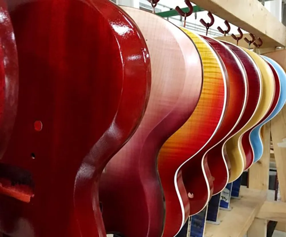A row of glossy colorful guitar bodies hangs in a workshop showcasing a variety of finishes