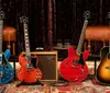 The image shows a collection of various electric guitars on display featuring different colors and designs with a reflective floor and large windows in the background of a music store