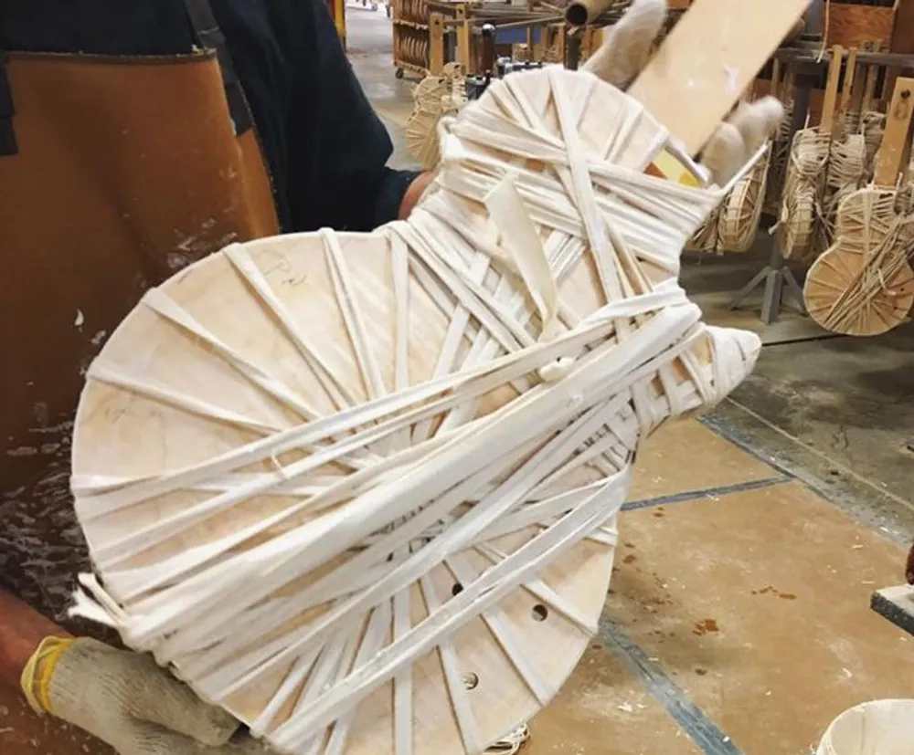The image shows the intricate framework of a piece of wooden furniture possibly a chair being constructed or repaired with a focus on its curved wooden slats and strapping in a workshop setting
