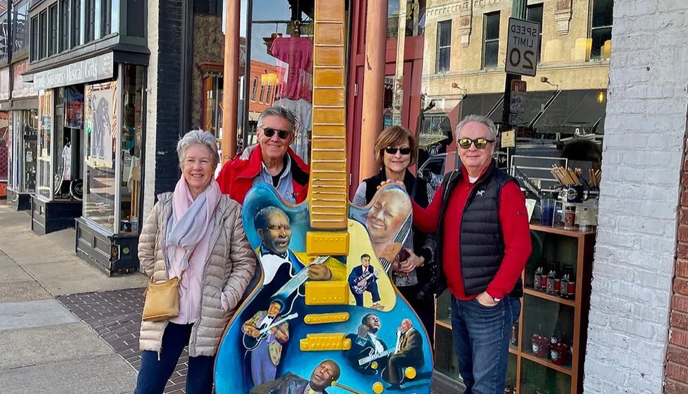 Four tourists are posing with a large guitar sculpture adorned with images of blues artists on a city street