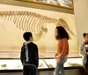 Several people including young visitors are observing the skeletal remains of a prehistoric creature on display in a museum exhibit