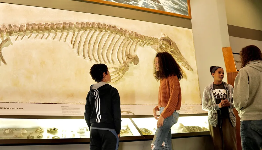 Several people including young visitors are observing the skeletal remains of a prehistoric creature on display in a museum exhibit