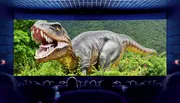 The image shows a movie theater from the perspective of the audience with a giant dinosaur displayed on the screen, creating an immersive cinematic experience.