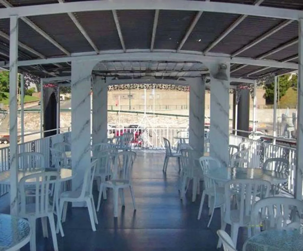 The image shows a covered outdoor seating area with white plastic chairs and tables on a deck overlooking a waterfront scene