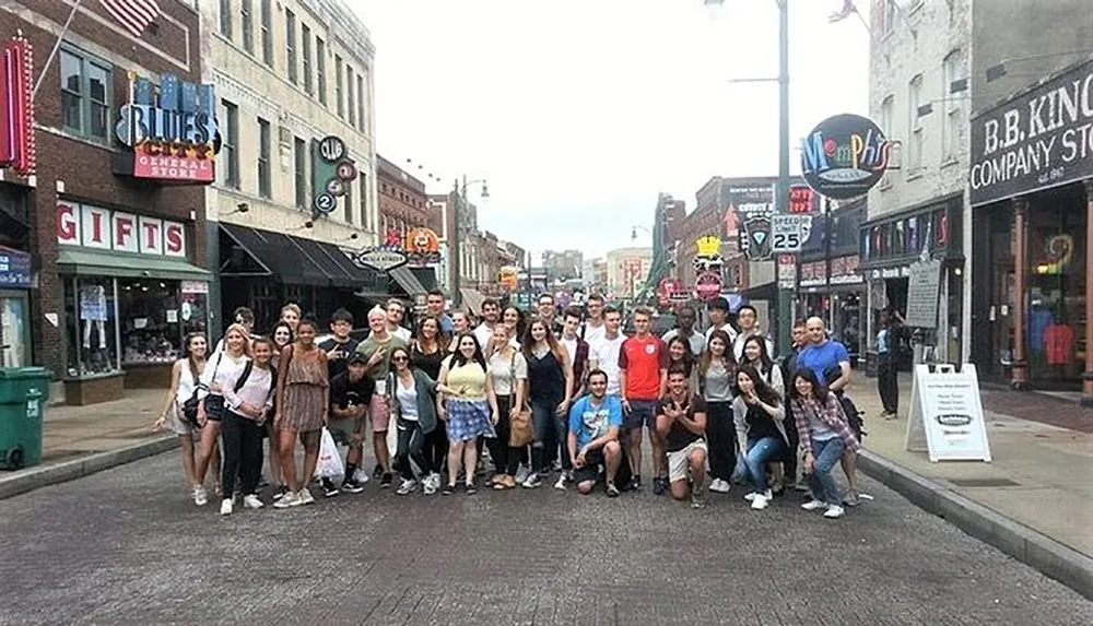 A diverse group of people poses for a photo on a street lined with music-themed stores and signs