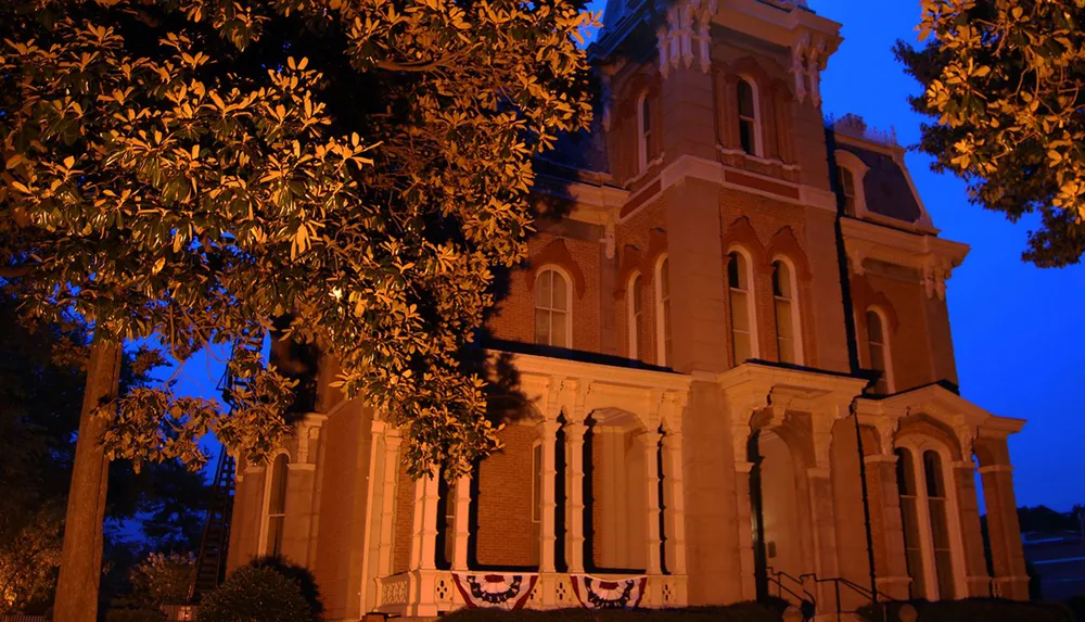 The image depicts a historic building illuminated by warm lights against a twilight sky surrounded by trees