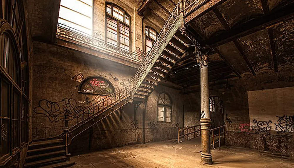 The image shows an abandoned dilapidated interior featuring a grand staircase sunlight streaming through windows with walls covered in graffiti