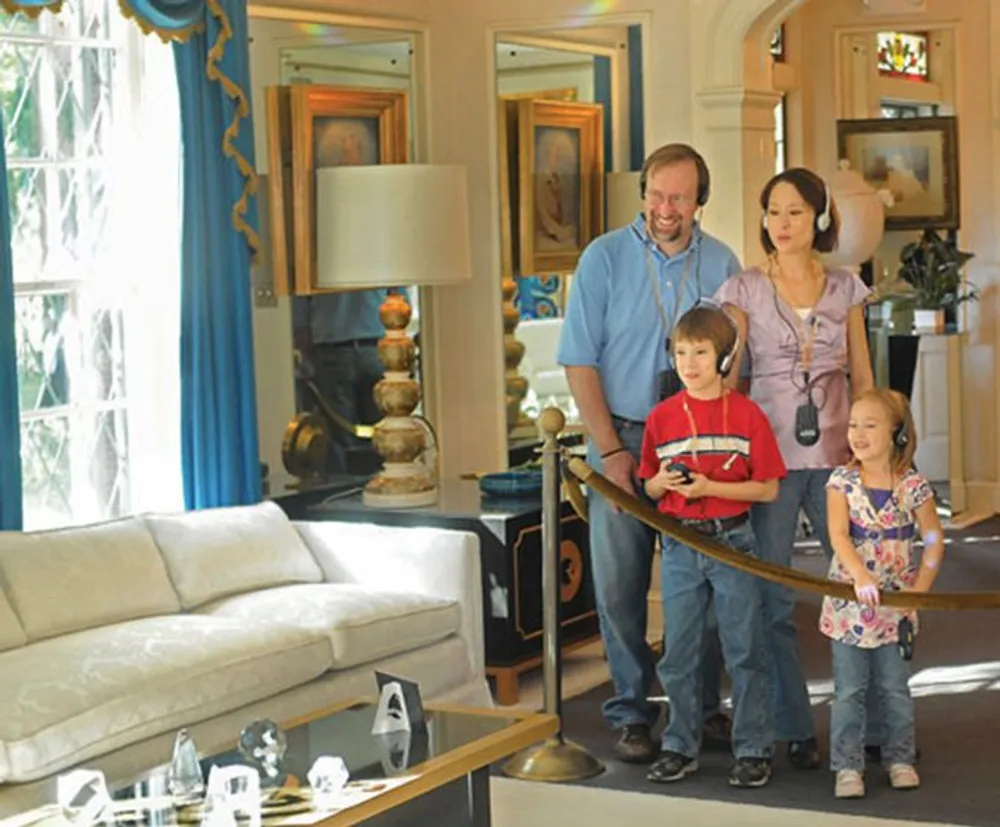 A family of four is observing a well-decorated room with two children wearing audio guides indicating they are likely on an audio-guided tour