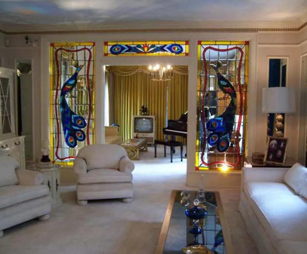 A luxurious room features an ornate stained glass peacock design on the doors white furniture a grand piano and vintage television set