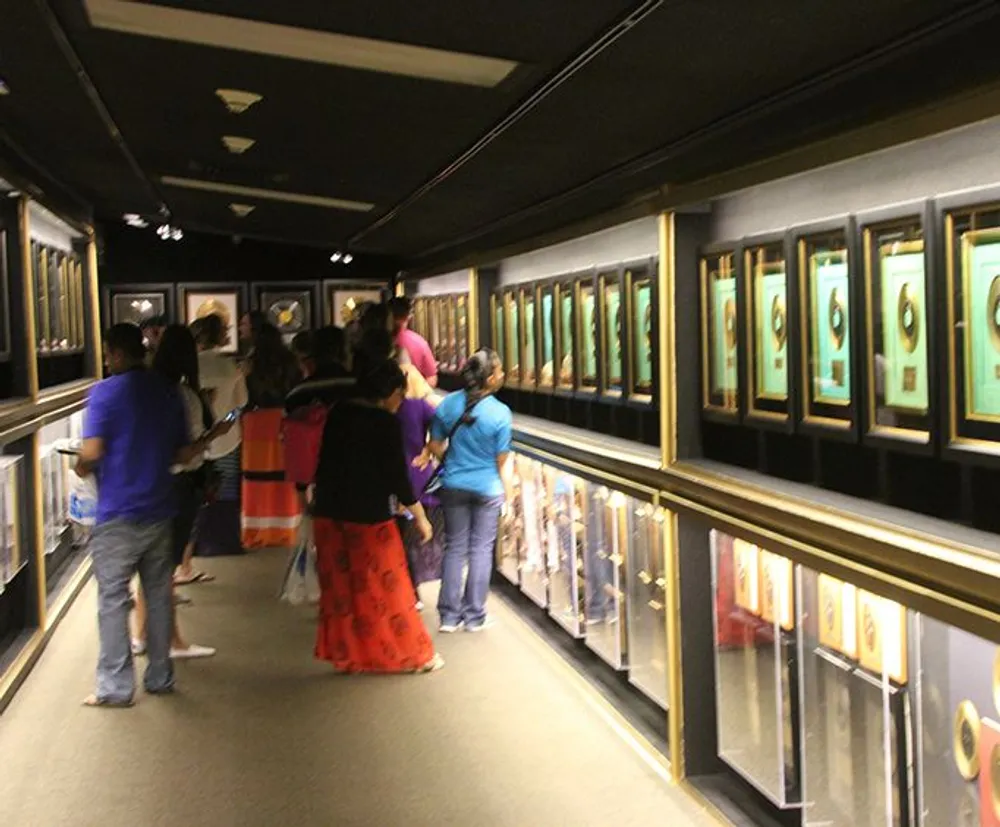 Visitors are viewing an exhibition with a series of framed artworks displayed on the walls of a dimly lit gallery corridor