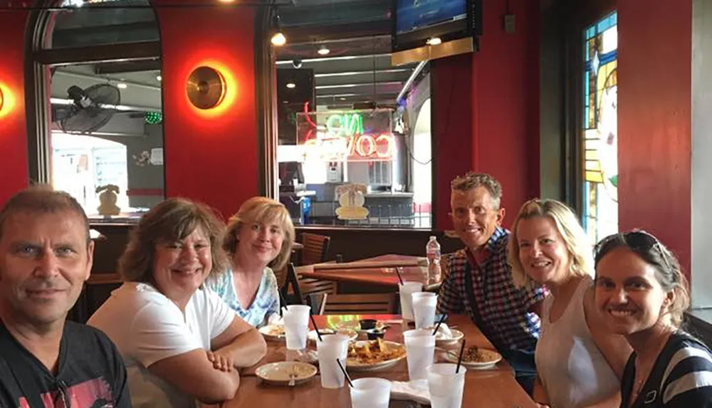 A group of six people are smiling at the camera while seated around a restaurant table with drinks and the remnants of a meal