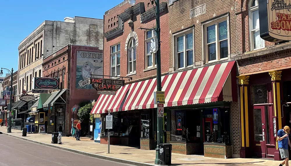 A sunny day on a historic downtown street showcasing a row of vintage-style buildings with colorful storefronts and striped awnings