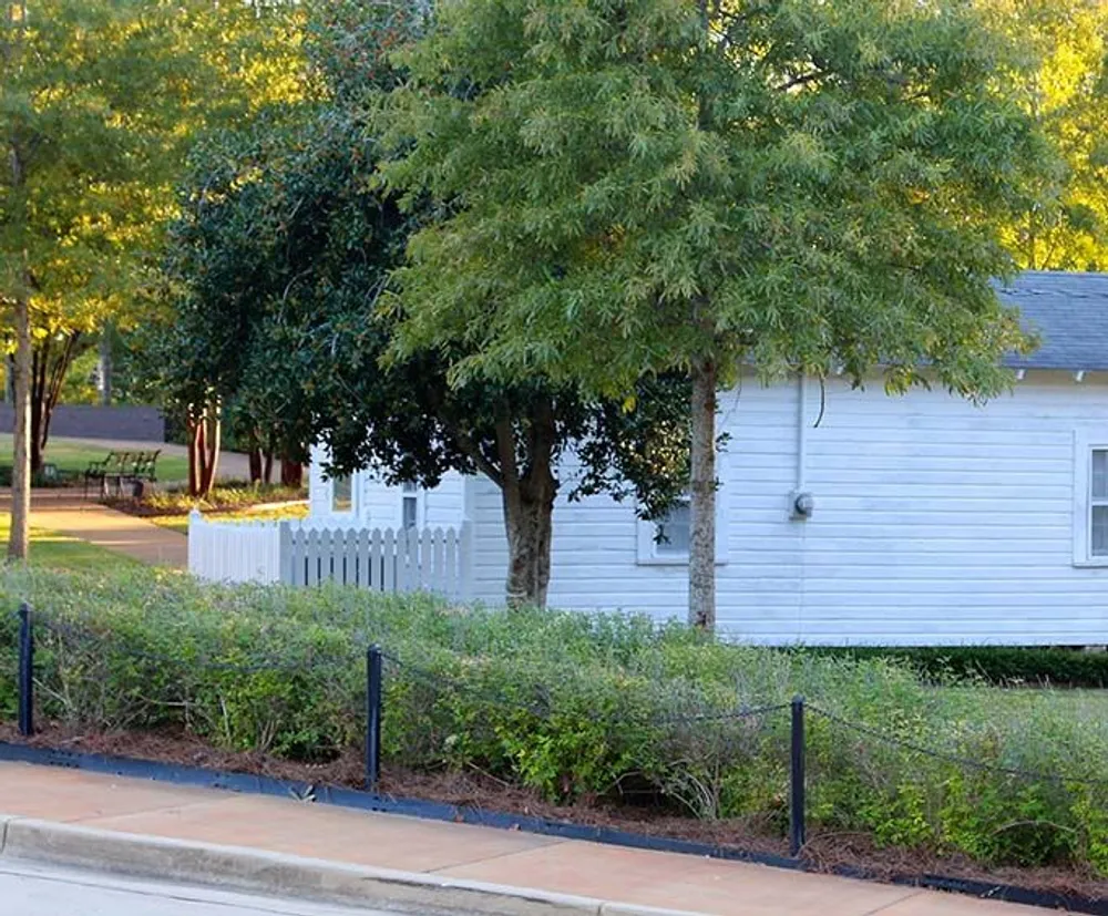 The image depicts a tranquil suburban scene with a white house with a picket fence surrounded by lush greenery