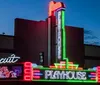 The image shows a brightly lit playhouse with colorful neon signs against a dark evening sky