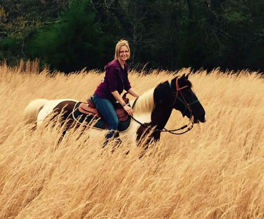 A person is smiling while riding a horse through a field of tall golden grass