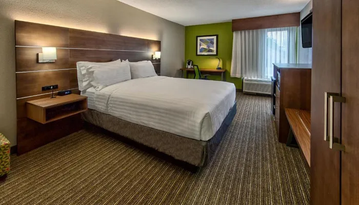 The image shows a neatly arranged hotel room with a large bed a desk area green walls and contemporary dcor