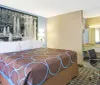 The image shows a neatly arranged hotel room with a large bed adorned with a patterned cover a big wall-mounted photograph of a fountain above the bed two bedside lamps and an adjoining desk area with a mirror and chair
