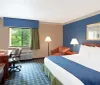 The image shows a neatly arranged hotel room with a bed work desk sitting area and a window overlooking greenery