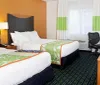 The image shows a neatly arranged hotel room with two double beds colorful bedding and a work area with a desk and chair
