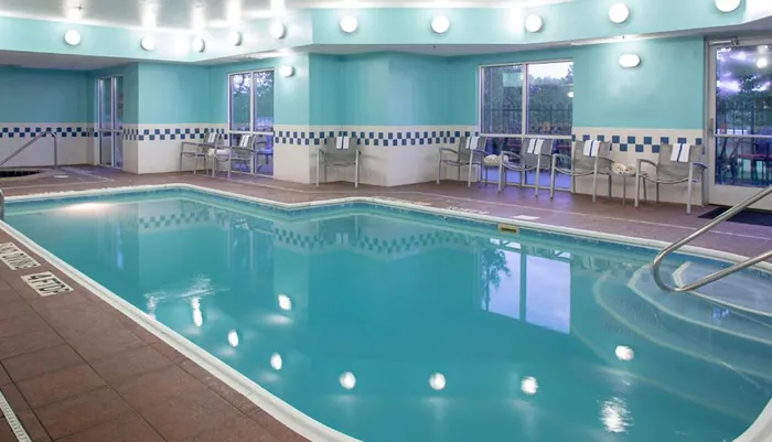 This is an image of a calm indoor swimming pool area with chairs around the periphery under a blue and white decor