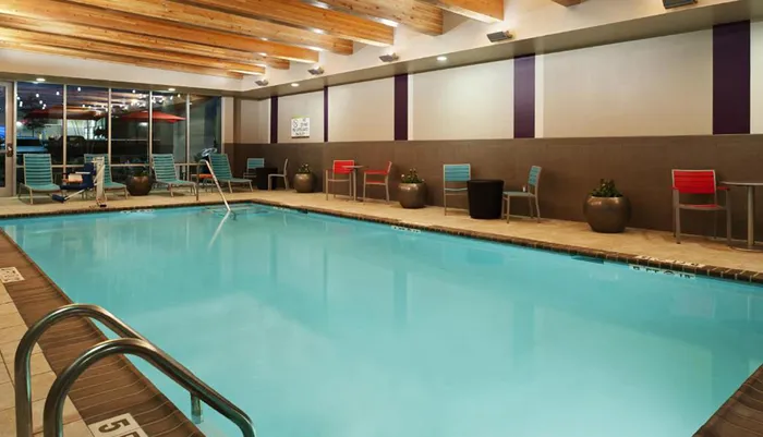 An indoor swimming pool with colorful chairs along the side and a wooden ceiling