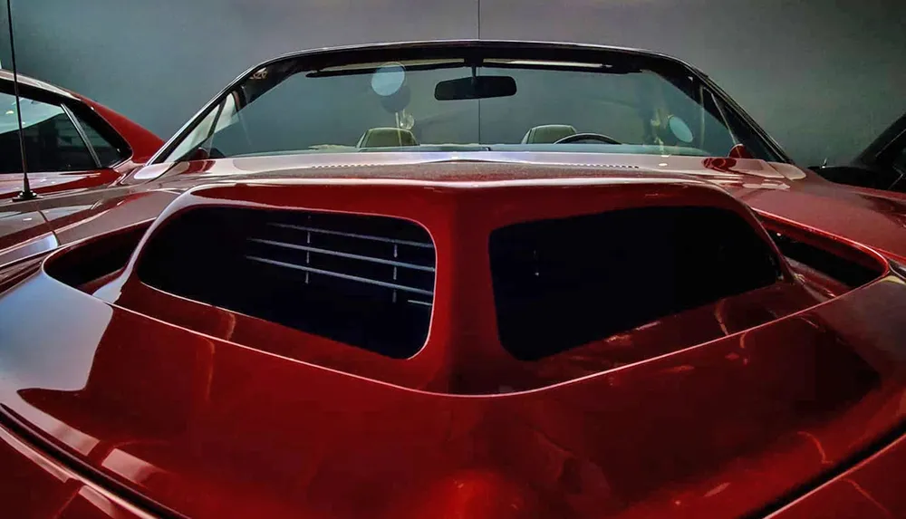 The image features a close-up rear view of a sleek red sports car with distinctive cooling vents and a roofline that slopes smoothly into the rear deck