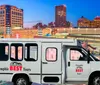 A tour van with Memphis BEST Tours on its side is parked with a backdrop of the Memphis skyline at twilight