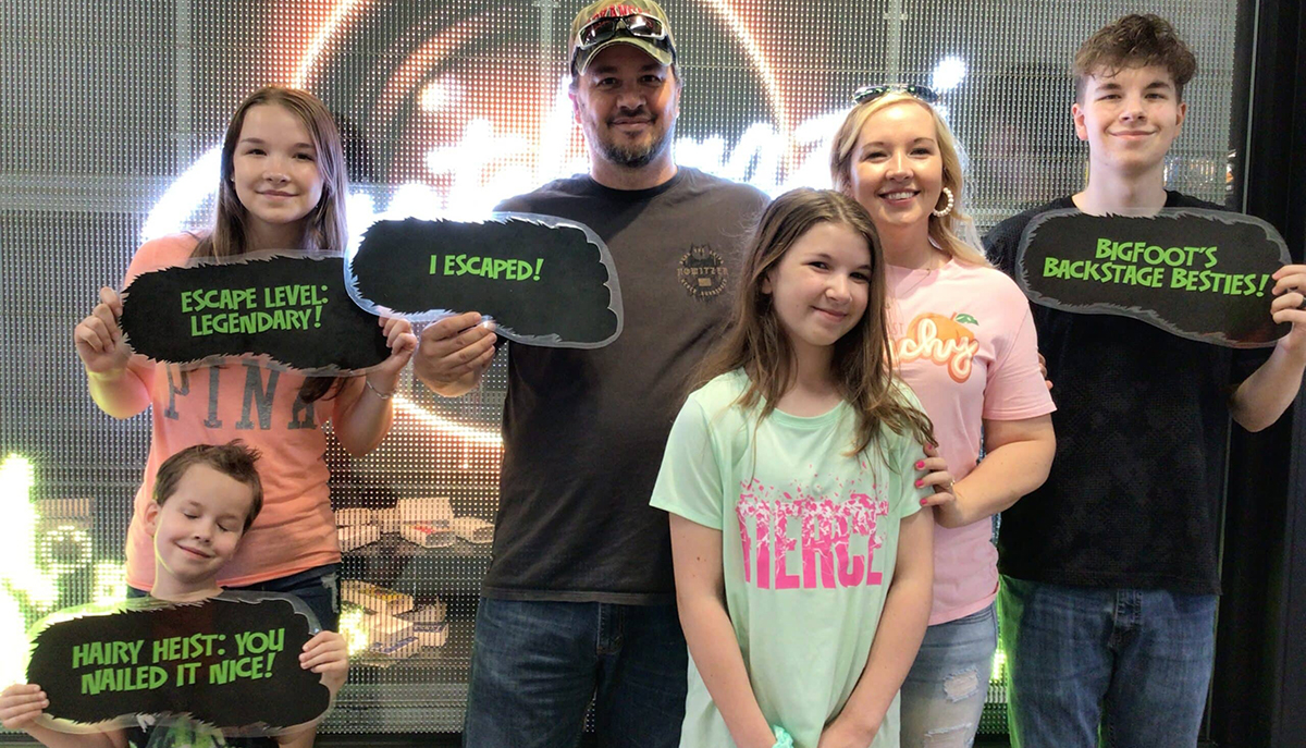 A group of six people is posing with signs celebrating their success in completing an escape room challenge.