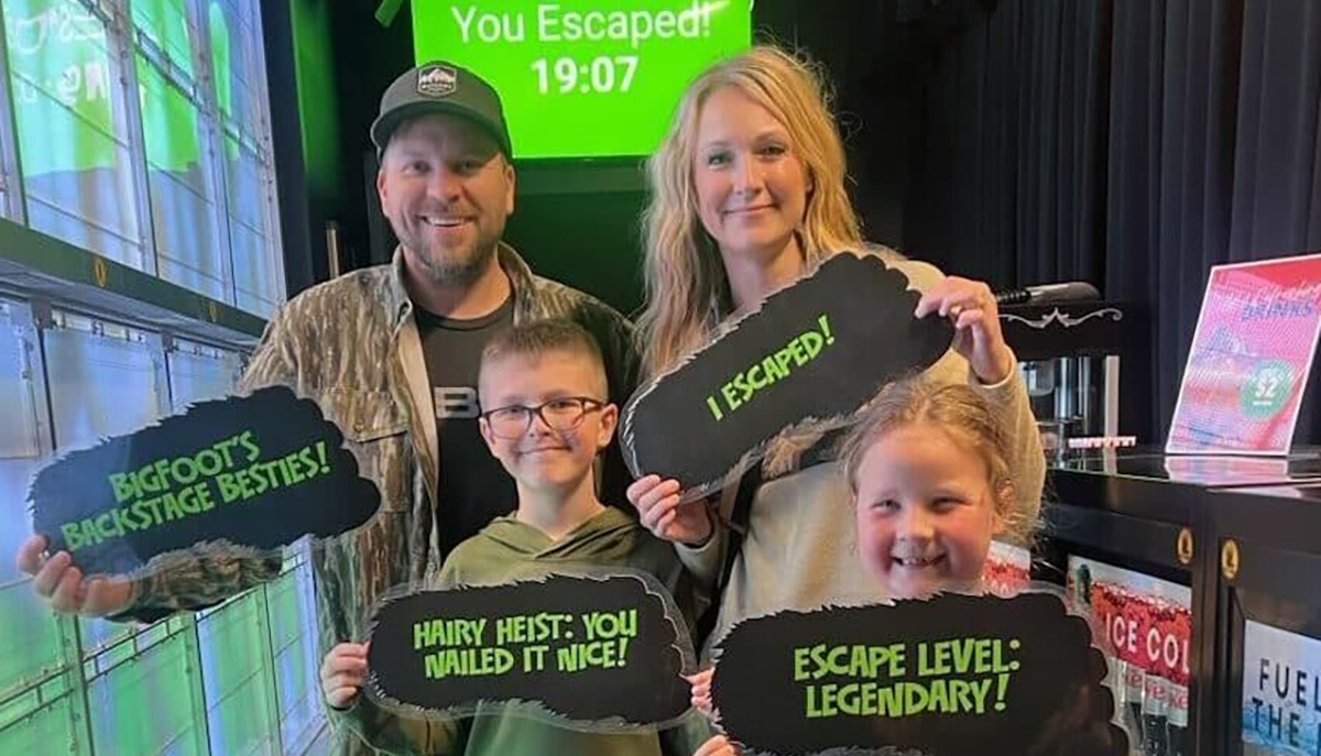 A family of four is happily posing with signs indicating they've successfully completed an escape room.