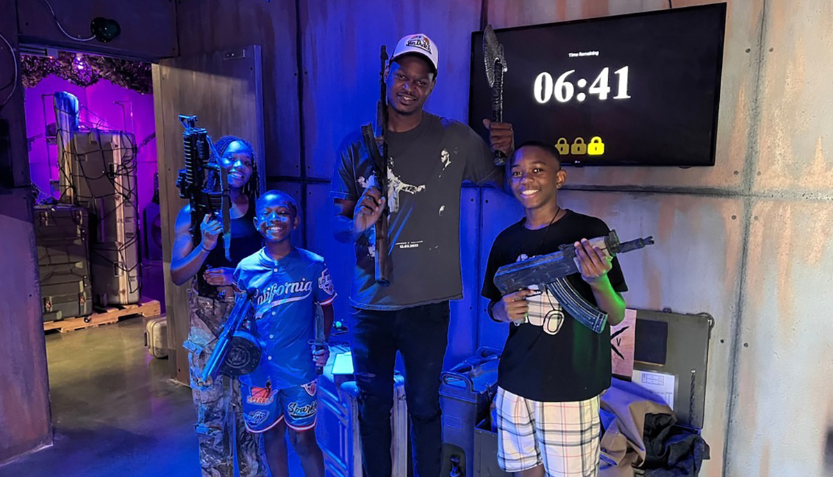 A group of people is posing with toy guns in a themed room, with a timer showing 06:41 on the wall behind them.