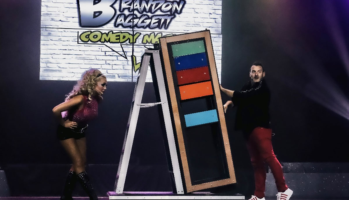 Two performers are on stage with a large colorful prop, under a sign that says 