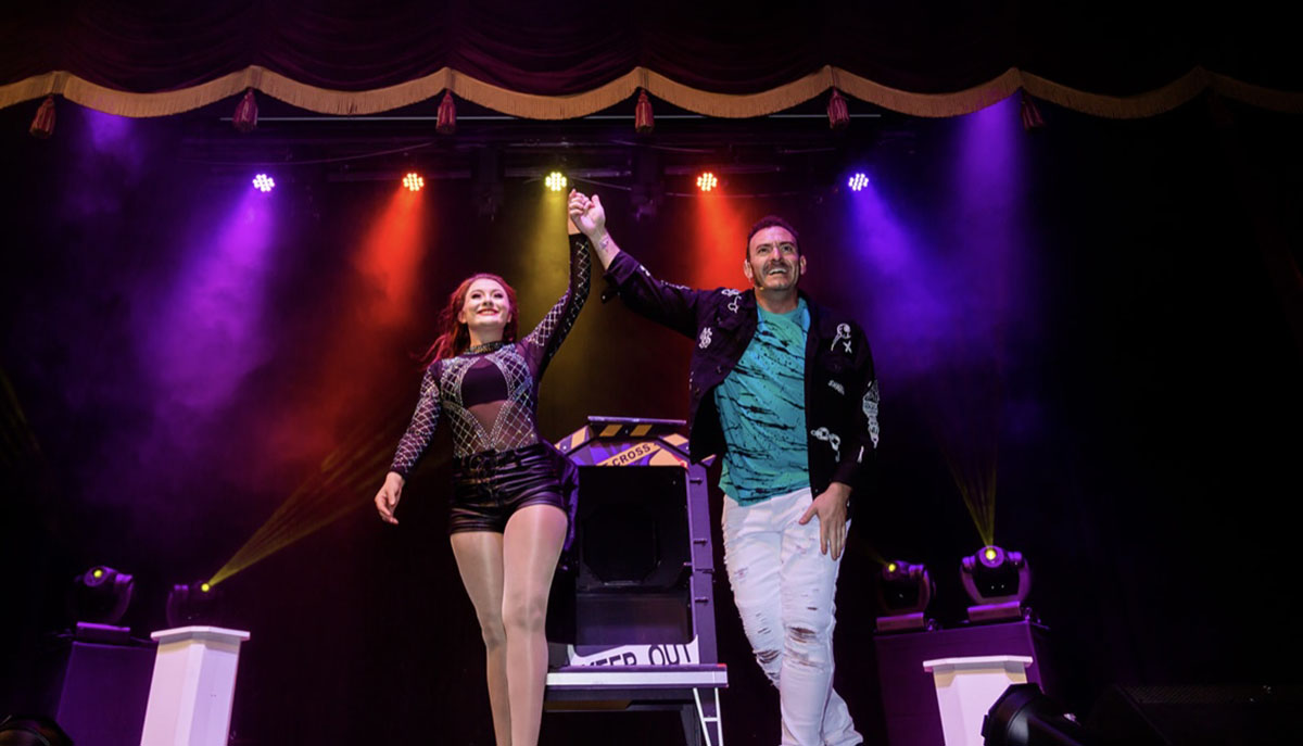 Two performers are taking a bow on stage under colorful lights.