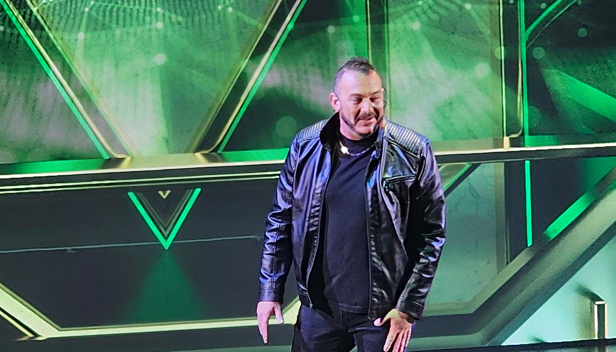 A person in a black leather jacket stands against a futuristic, green-lit background.